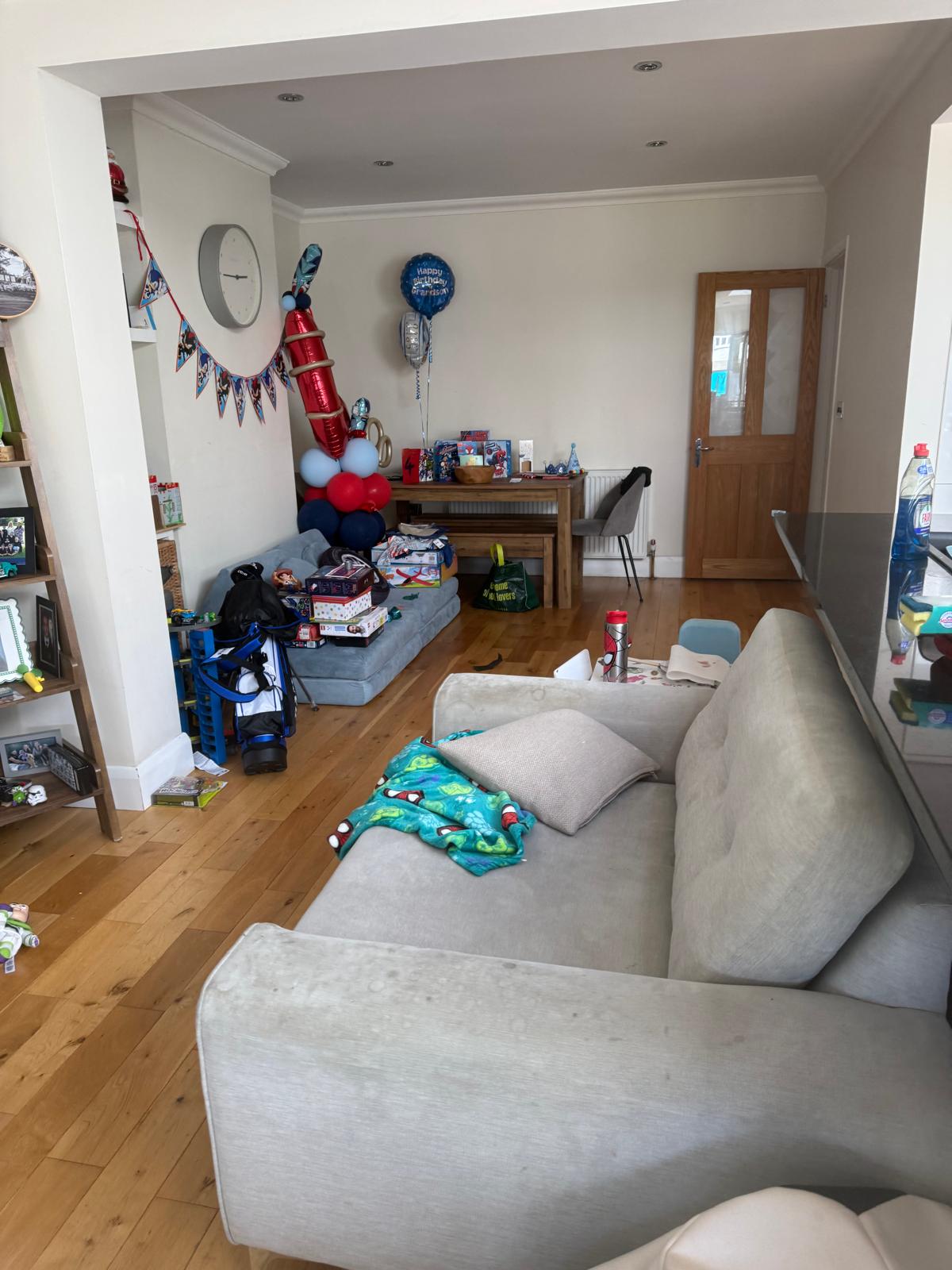 Open-plan dining and living room before organising, with toys, party decorations and clutter across the floor