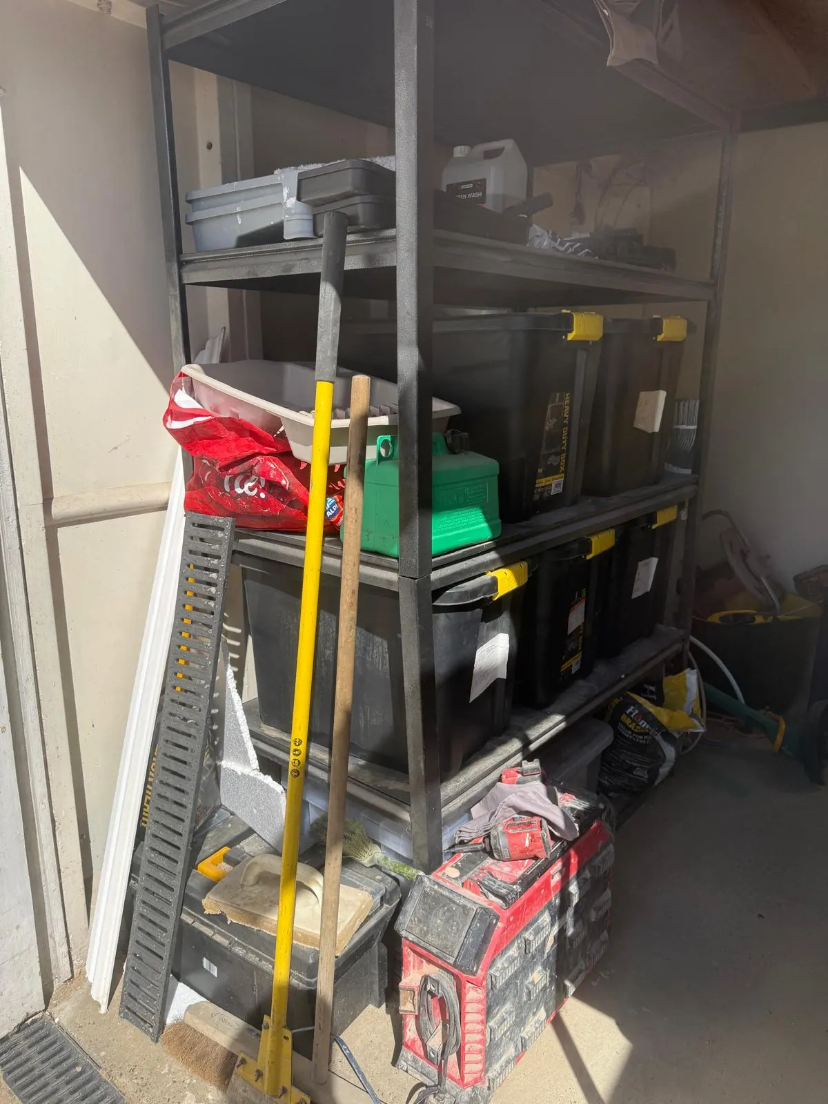 Garage shelving before organising, with tools, boxes and bags piled across the racking