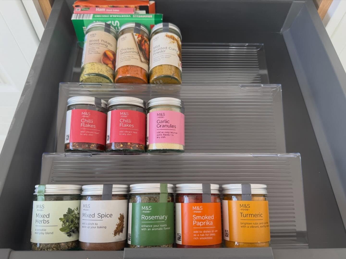 Space-planned spice drawer with tiered clear risers and labelled jars in easy reach
